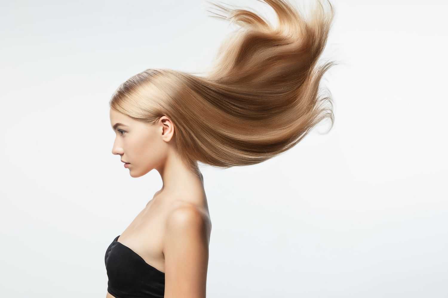 Side profile of a woman with long, flowing blonde hair in a black strapless top against a white background.