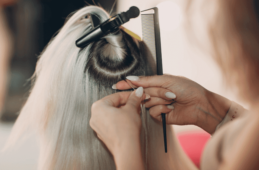 Stylist using a comb and hair clip to section and straighten long, blonde hair in a salon.
