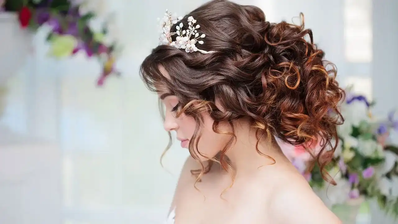 Bride with curly hair, adorned with a floral hair accessory, standing amidst colorful flowers.